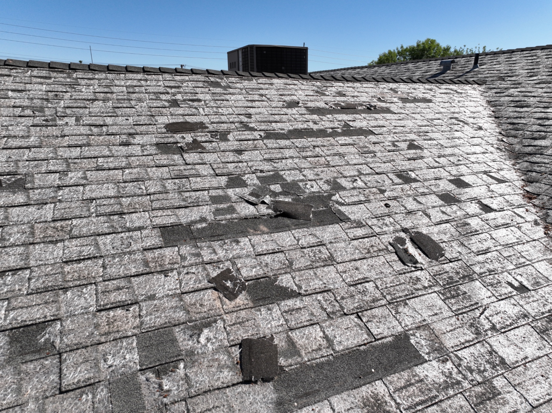 Missing and lifted shingle tabs with prior handyman patches on Mesa AZ roof