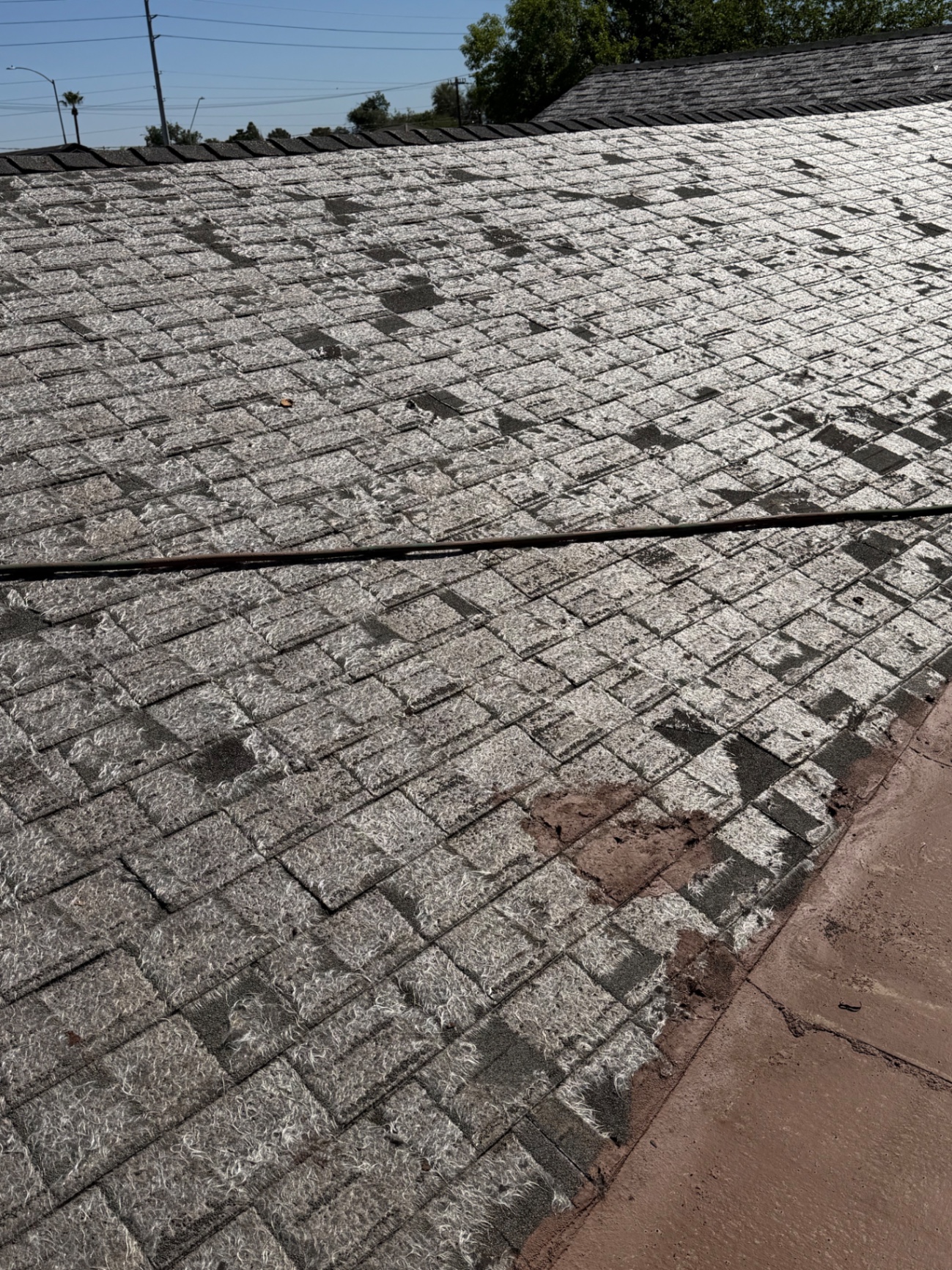 Heavily patched asphalt shingle field next to failed flat roof coating